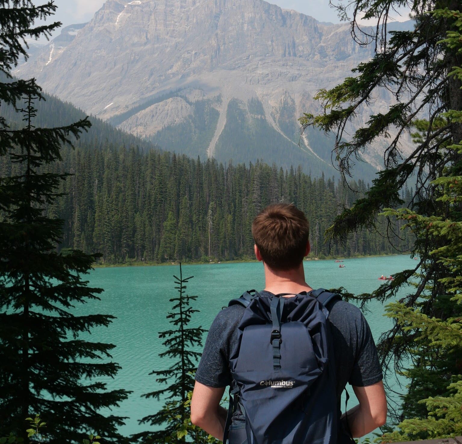 hiker with backpack overlooking turquoise lake and mountains