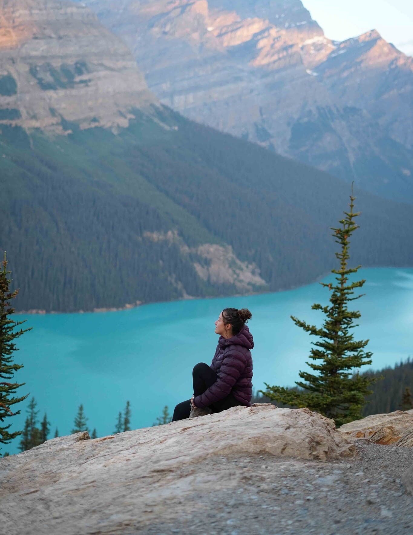 woman in purple jacket looking at turquoise lake and mountains